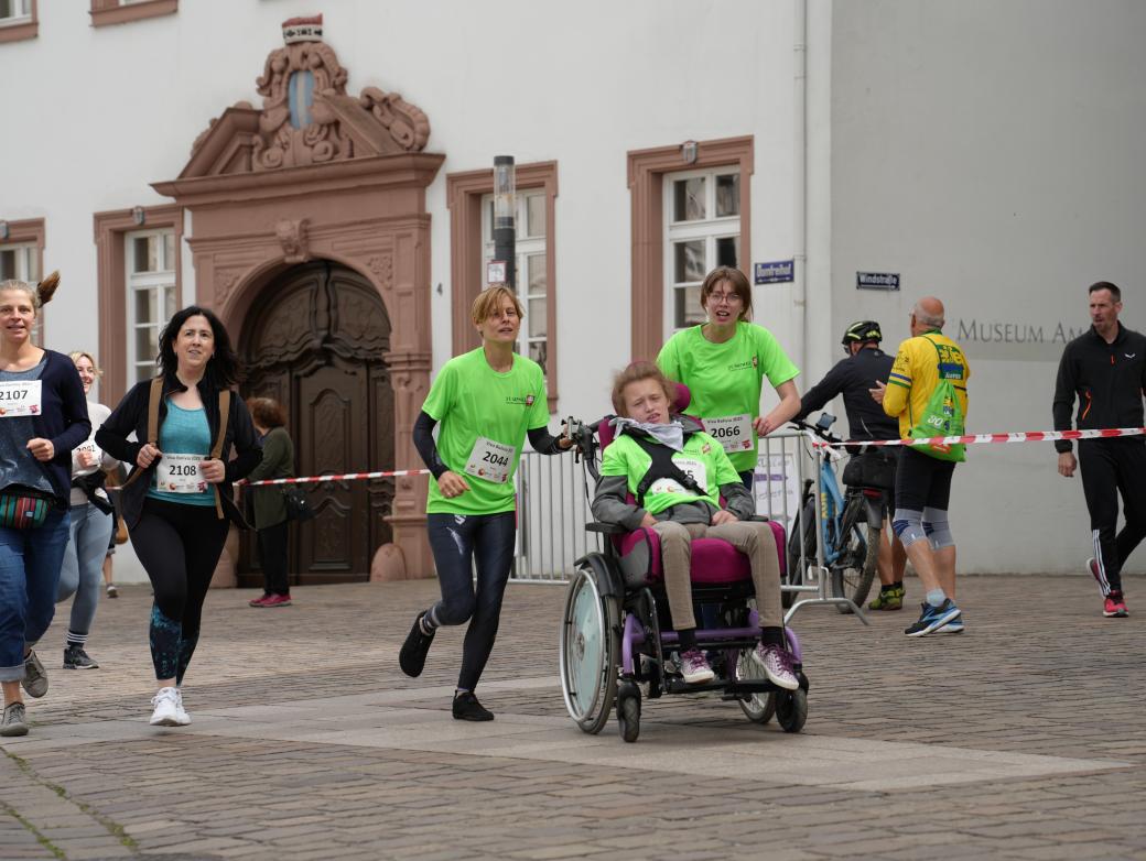 Fünf Menschen, davon eine Person im Rollstuhl, laufen über die Strecke