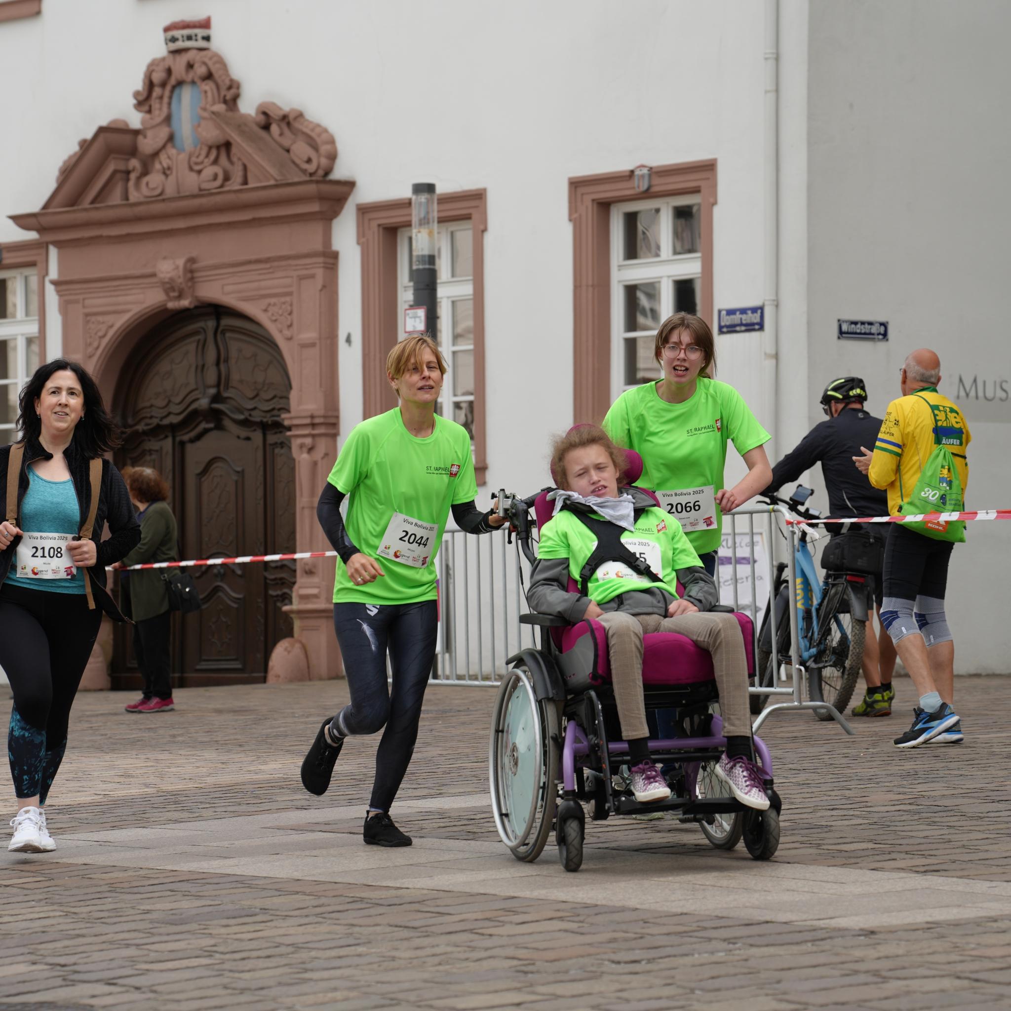 Fünf Menschen, davon eine Person im Rollstuhl, laufen über die Strecke