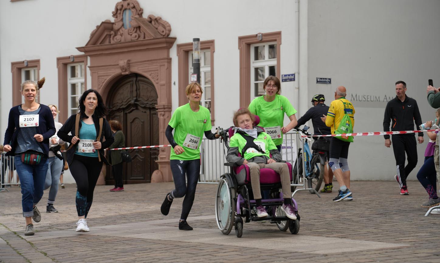 Fünf Menschen, davon eine Person im Rollstuhl, laufen über die Strecke