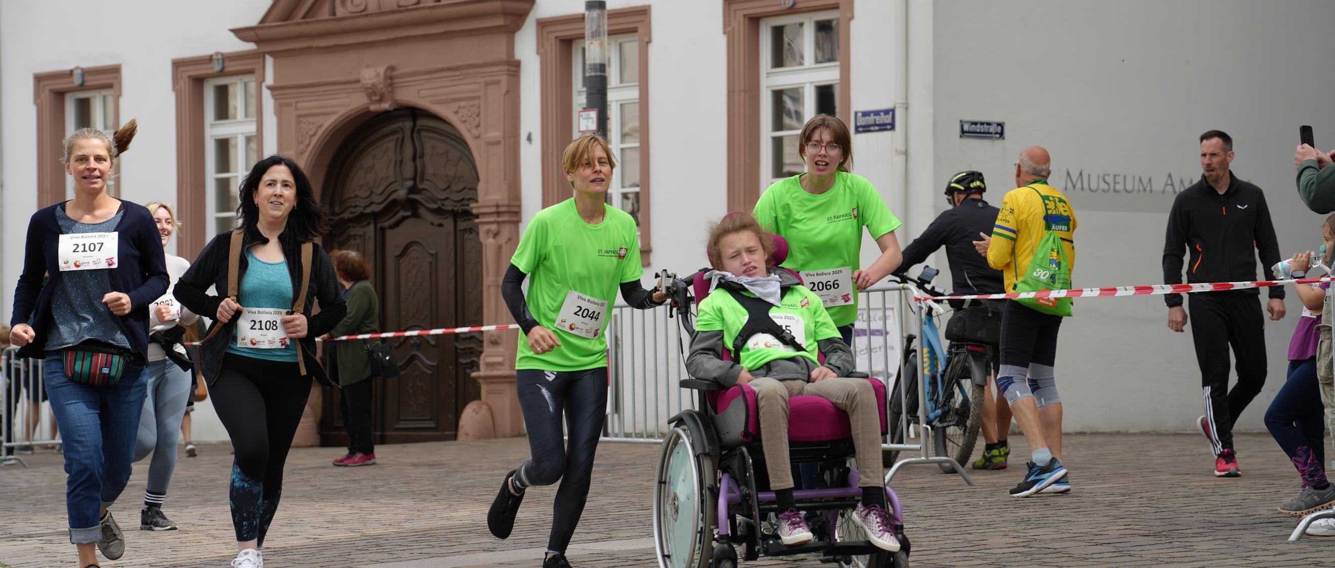 Fünf Menschen, davon eine Person im Rollstuhl, laufen über die Strecke